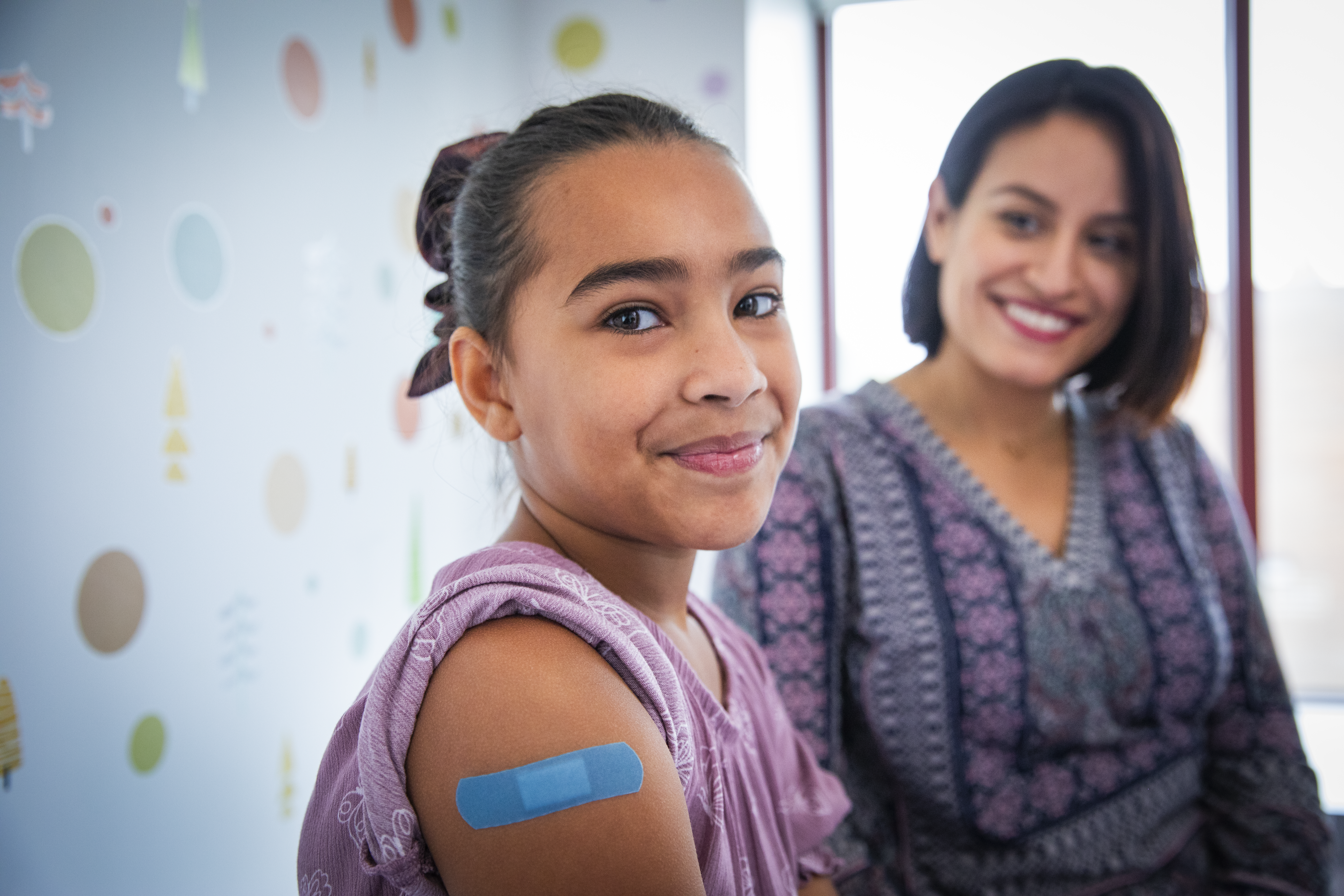 Pediatric Patient with Parent at Doctor's Office Pediatric Patient smiling with parent at doctor's office with band aid on upper arm.
