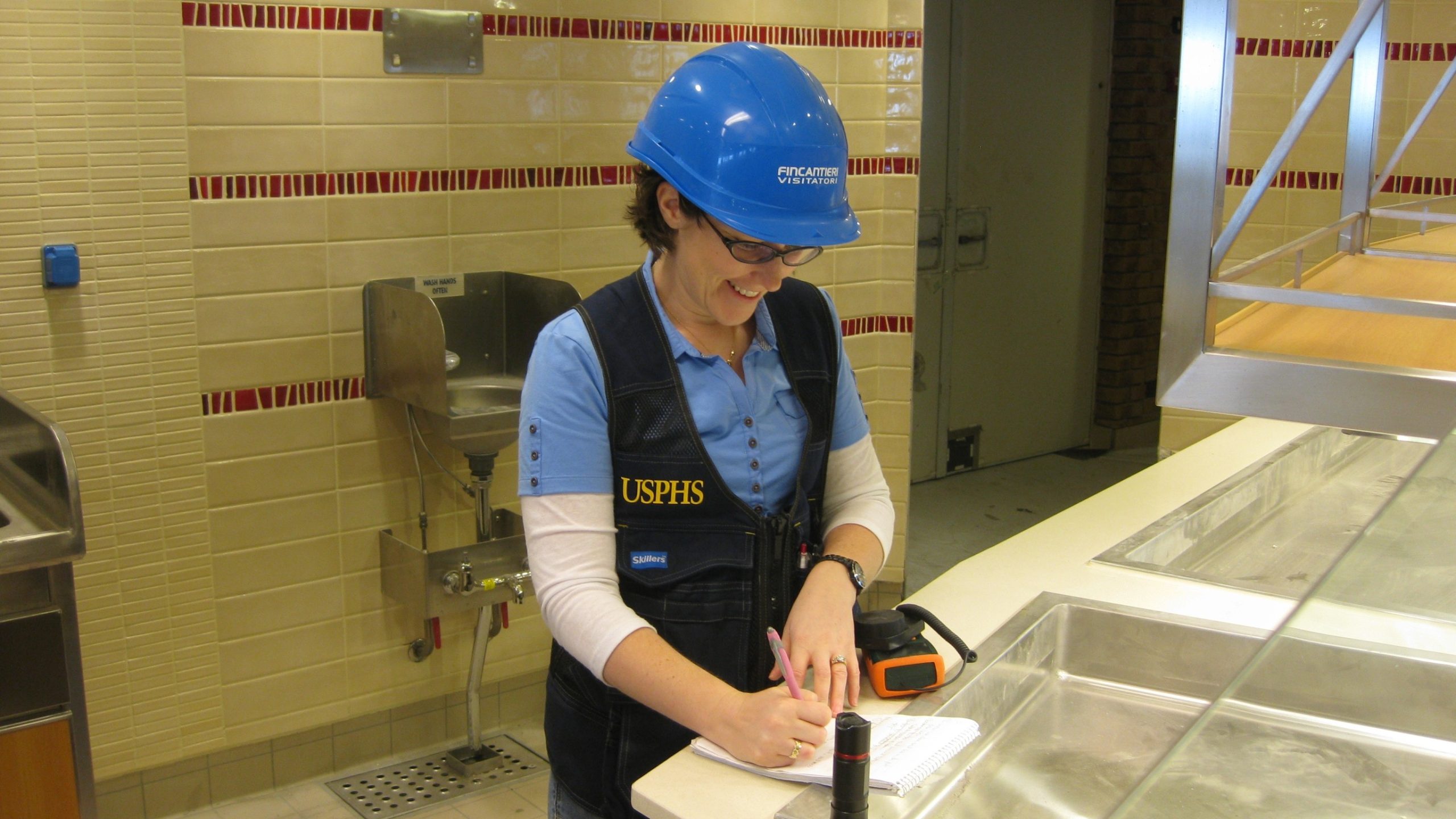 Construction inspections Public health officer wearing a hard hat taking notes on a clipboard inside a galley.
