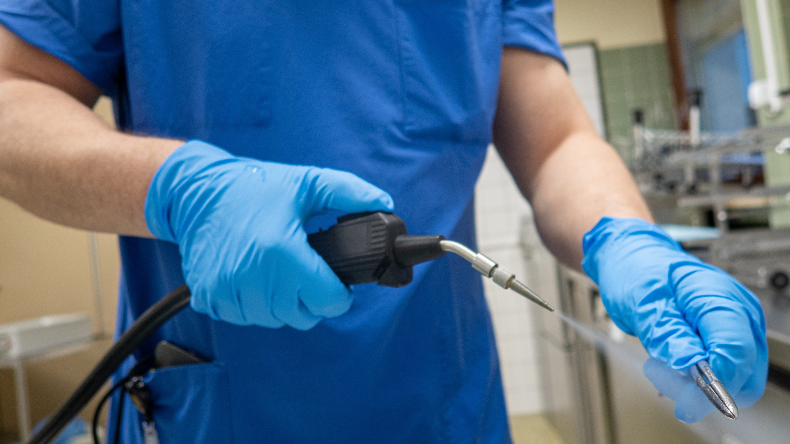 EWSP image resized A doctor's hands wearing blue sterile gloves while sanitizing a medical instrument with pressurized water.