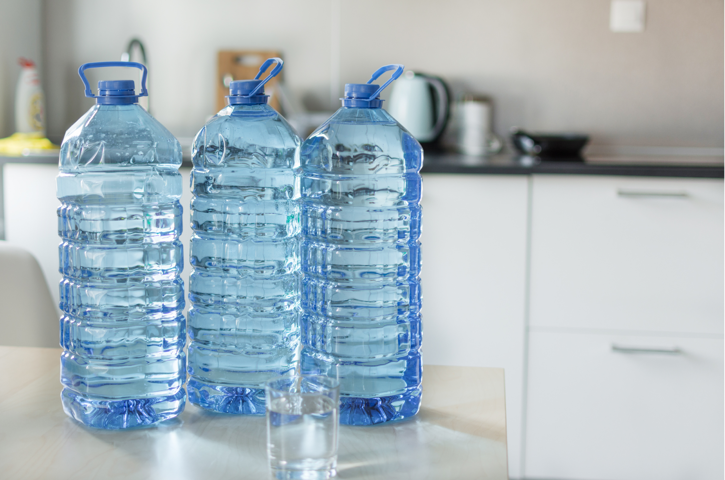 Foto de tres botellas grandes transparentes con agua sobre la mesa con un trasfondo de cocina. Foto de tres botellas grandes transparentes con agua sobre la mesa con un trasfondo de cocina.