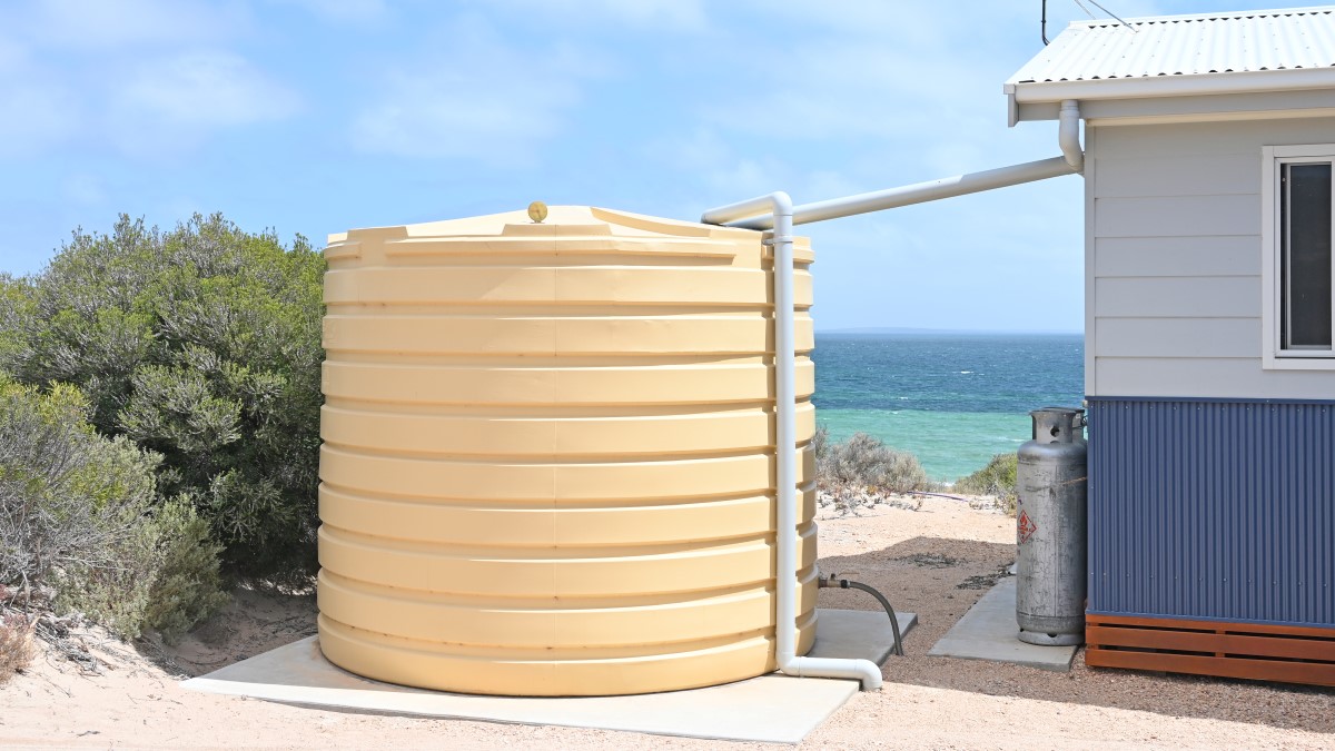 Tanque de almacenamiento de agua de plástico grande (cisterna) sobre una base de concreto. Tanque de almacenamiento de agua de plástico grande (cisterna) sobre una base de concreto. Un tubo de plástico conecta la cisterna a una manguera. Otro tubo de plástico va desde la cisterna hasta el suelo. Se ve que la cisterna y la casa están al lado del mar.