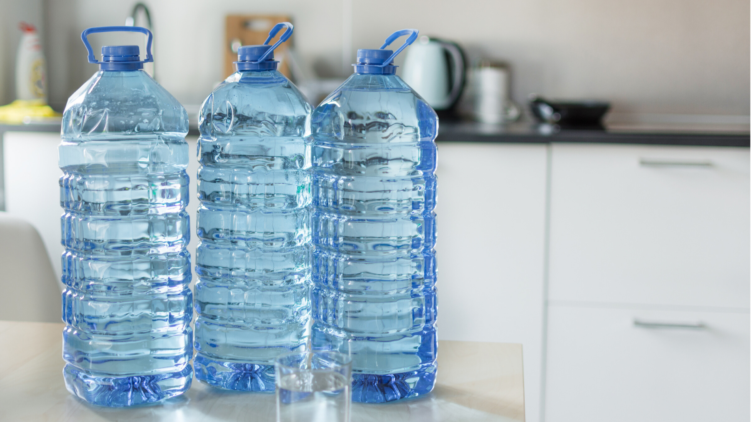 3 clear plastic water bottles Picture of three clear transparent plastic bottles with water on the table over kitchen background