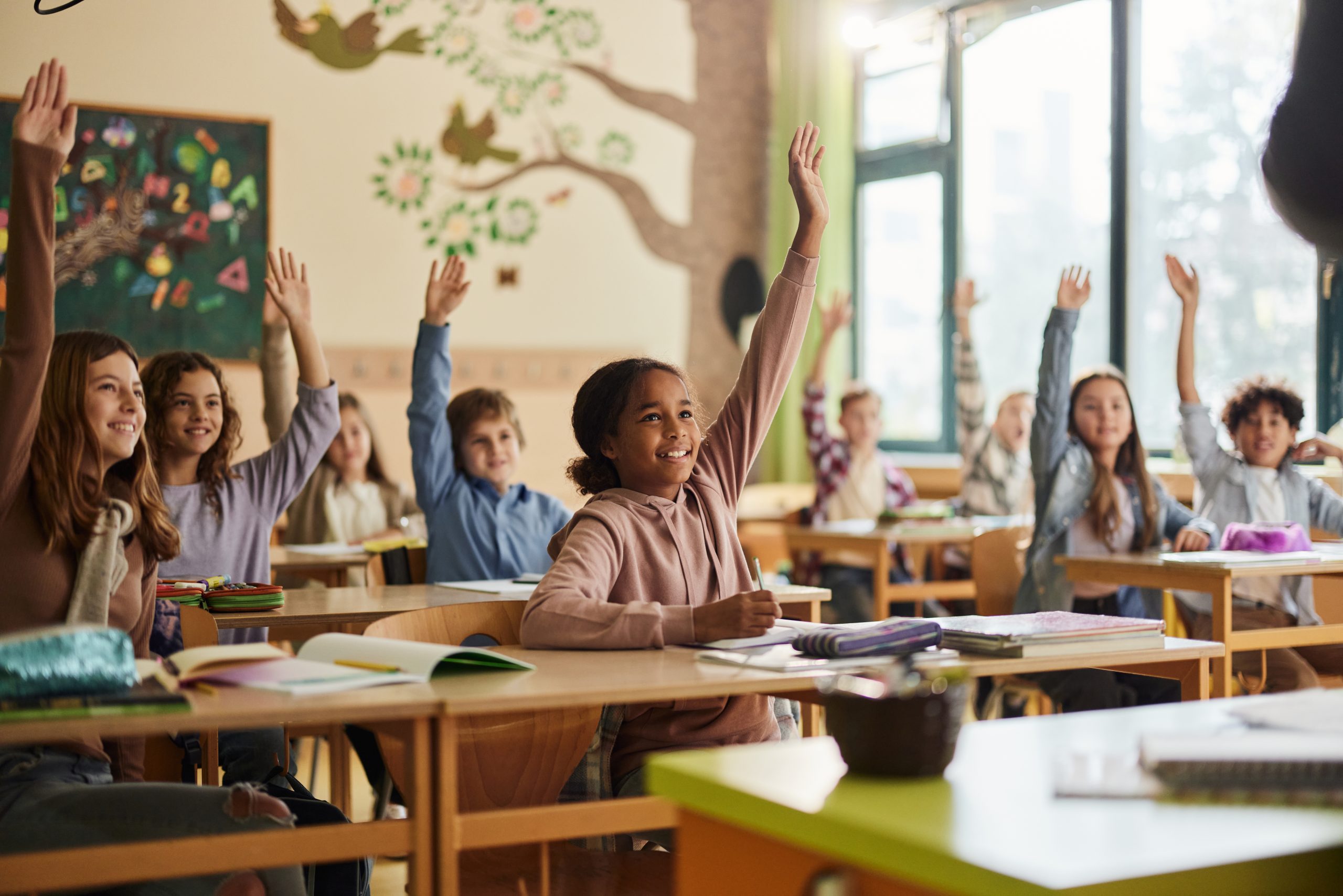 Happy elementary school students raising their hands during a class. Happy elementary school students raising their hands during a class.