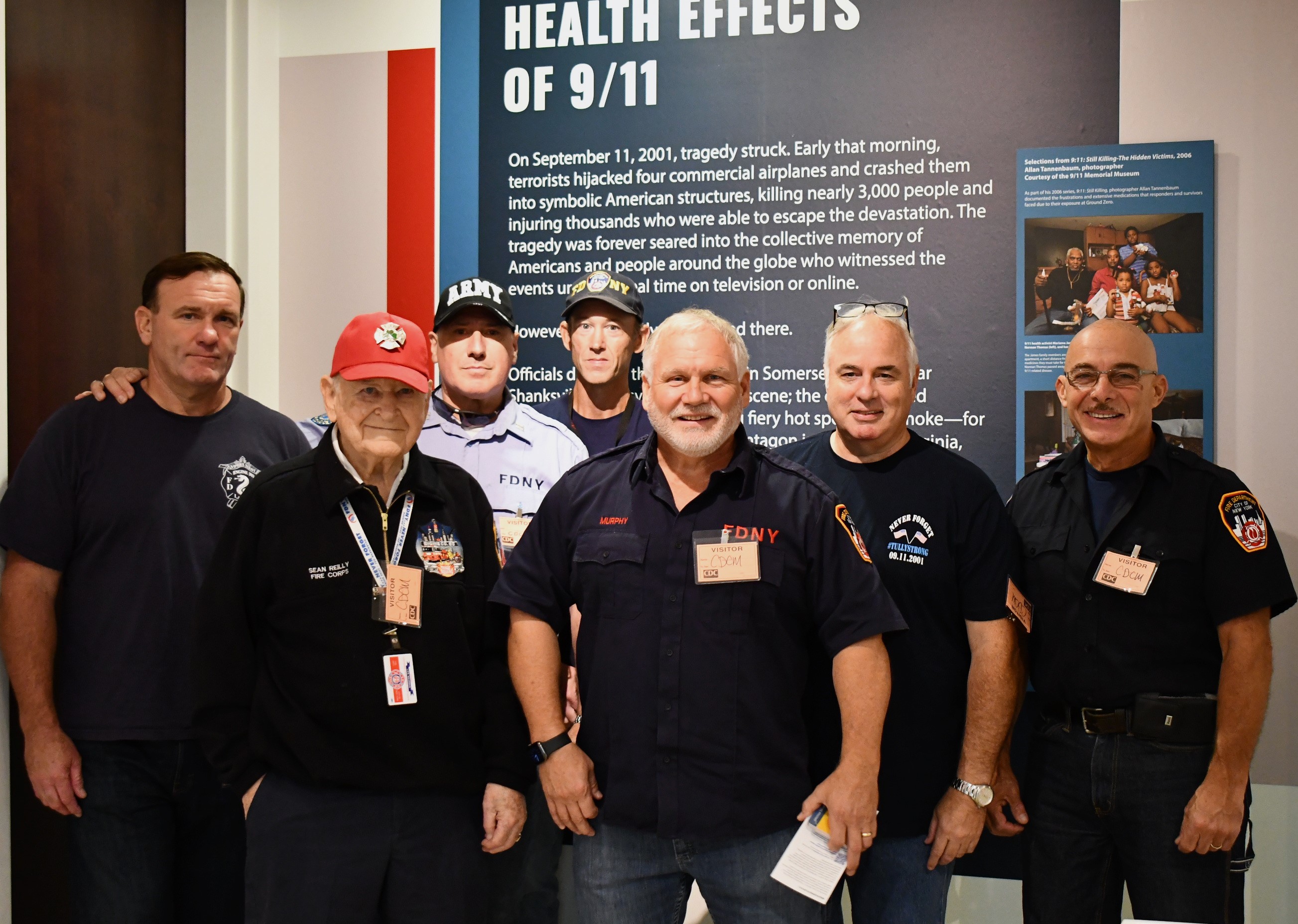 Tim Murphy, retired NYC firefighter and WTC Health Program member, stands proudly with a group of fellow 9/11 responders who are members of the NYC Shields of Georgia, a organization founded by Tim. The joyous group is captured with smiles during a memorable moment at the Health Effects of 9/11 exhibition at the CDC museum, embodying strength, camaraderie, and resilience.