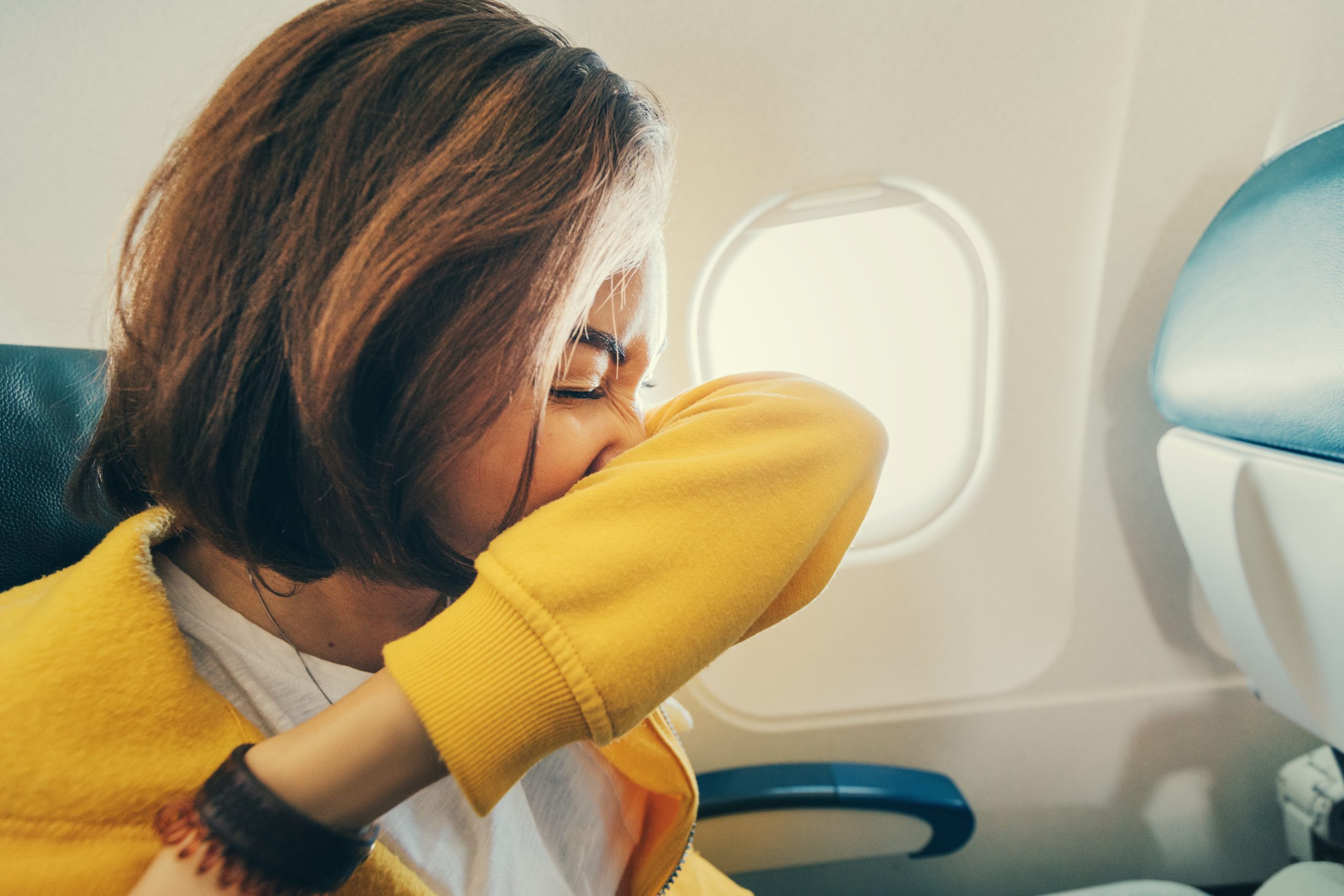 Traveler sneezing into arm on a plane.