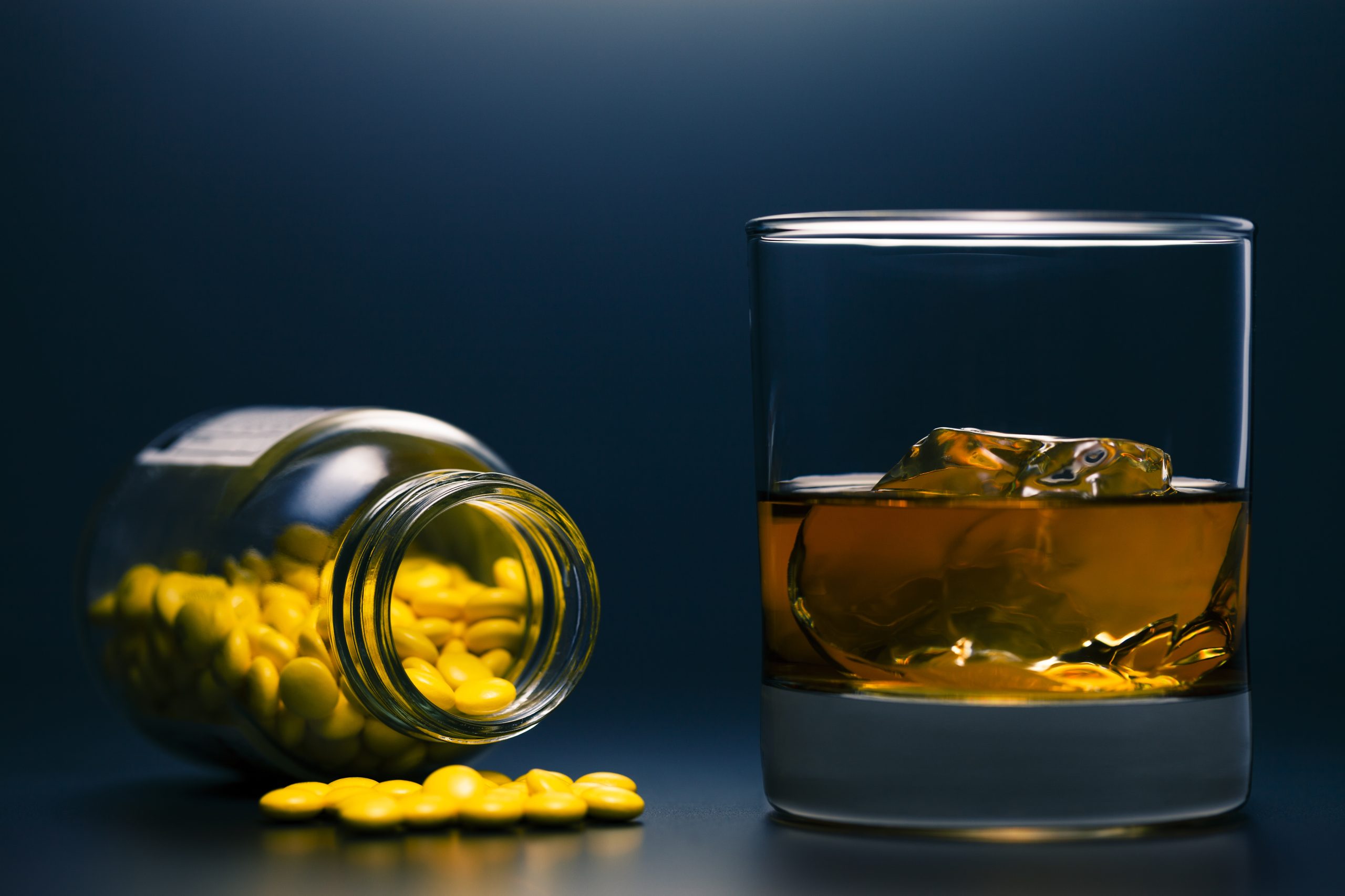 A bottle on the left with medication and a glass of alcohol on the right.