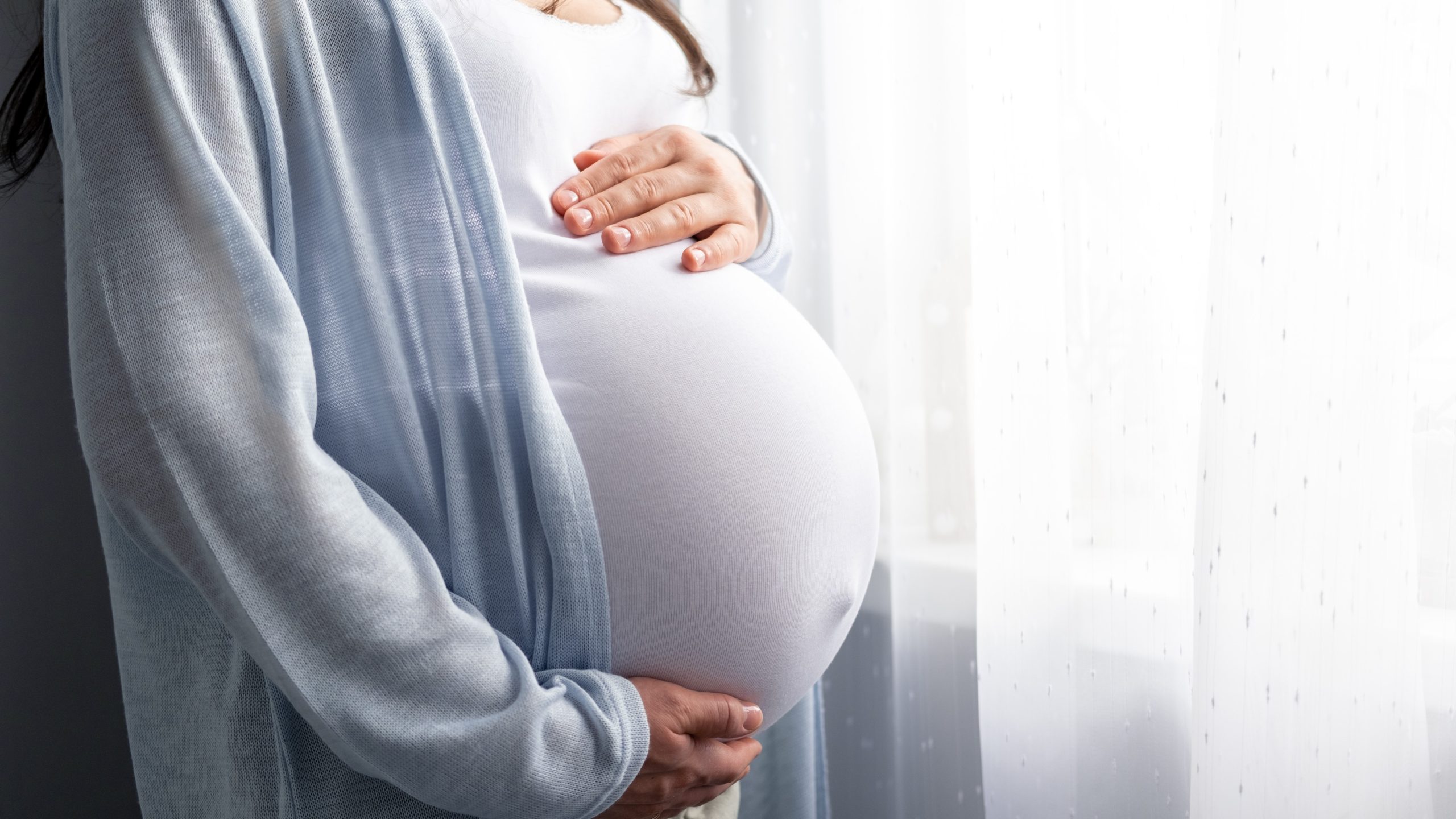 Pregnant person with hands on their abdomen Pregnant woman with hands on their abdomen.