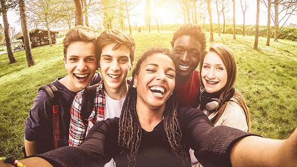 Sexual Risk Behaviors Five teenagers in a park smiling as they take a picture of themselves.