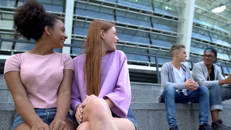 Sexual Risk Behaviors Two female teenagers sitting next to each other and looking over their shoulders at two male teenagers.